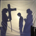 Schatten von erwachsenen Person und Kindern hinter einer Leinwand mit Kreuz